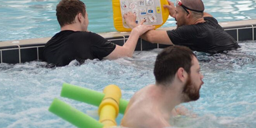 Three men enjoying some leisure time in the pool. Two of them are chatting using a communication display stuck on a kick board.