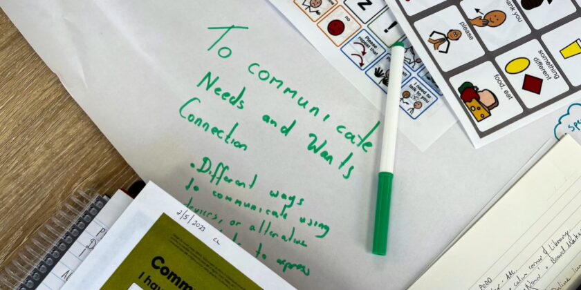 variety of Aided Language Display (ALD) sheets with a piece of paper in the centre that has writing on it in green texta pen, "to communicate needs and wants, connection,different ways to communicate".