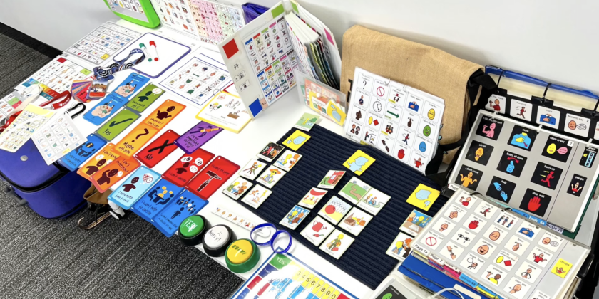 table with various Augmentative and Alternative Communication (AAC) tools and devices laid out on display