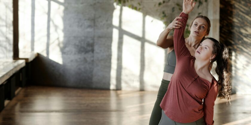 SUPPORT WORKER HELPING PERSON WITH DOWN SYNDROME IN A DANCE STUDIO WITH MOVEMENTS