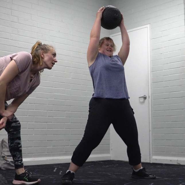 person at the gym with a medicine ball held over their head