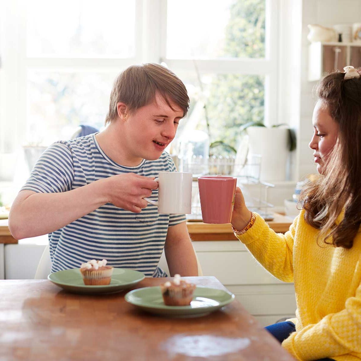 A young man with Downs syndrome drinking tea with a friend